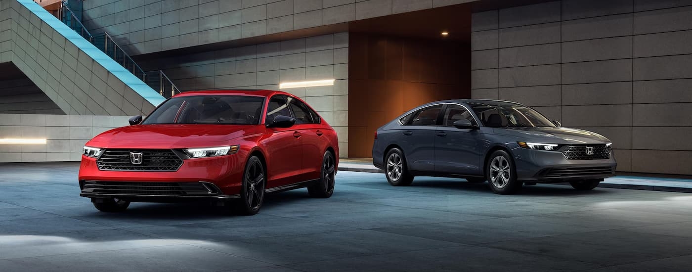 A red and a grey 2024 Honda Accord Sport Hybrid are parked near a set of stairs.