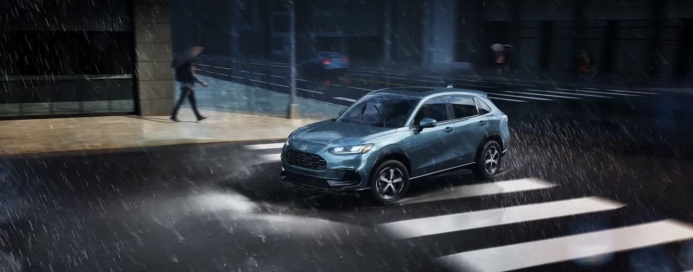 A blue 2023 Honda HR-V EX-L is shown driving through a rainy intersection.