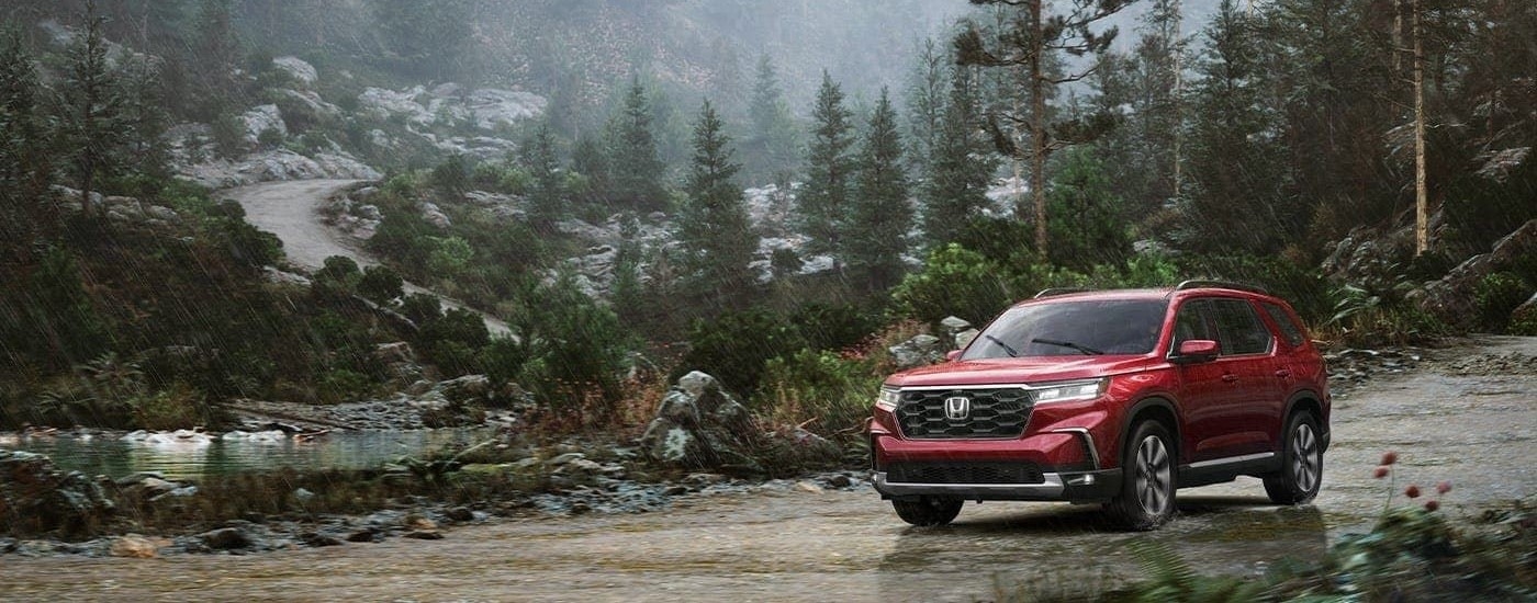 A red 2023 Honda Pilot Elite is shown on a rainy trail after looking at Honda SUVs for sale.