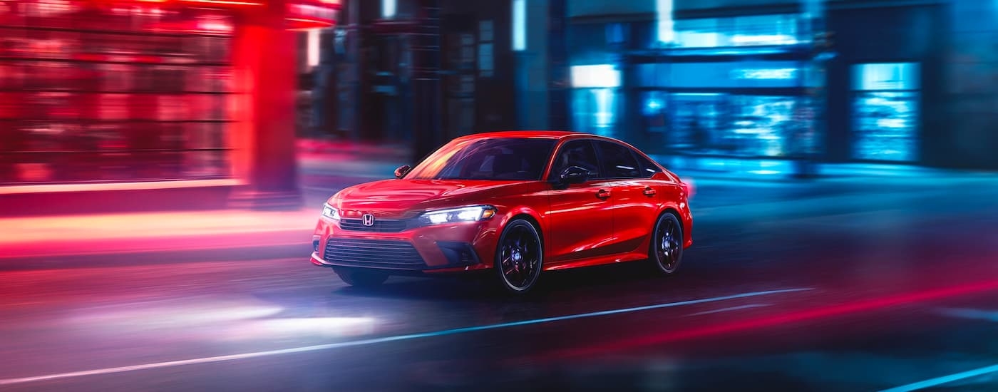 A red 2024 Honda Civic Sport is shown driving on a city street at night.