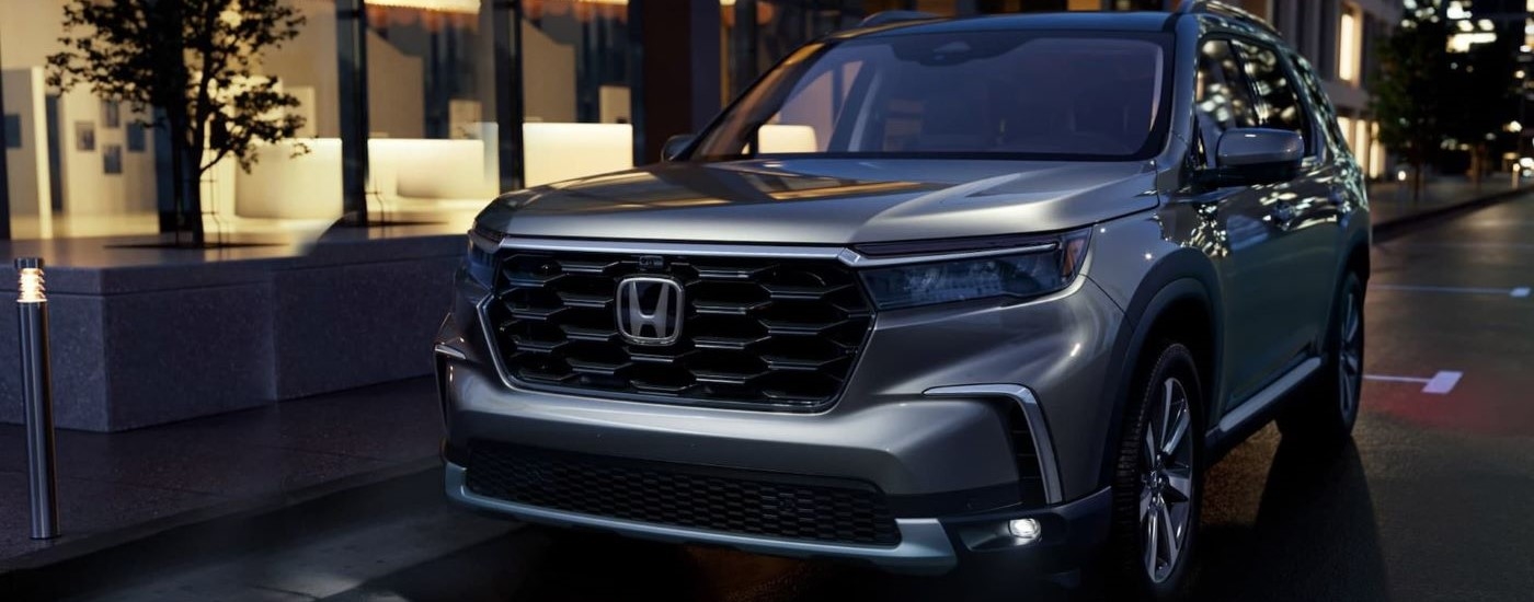 A silver 2023 Honda Pilot for sale is shown parked near a building at night.