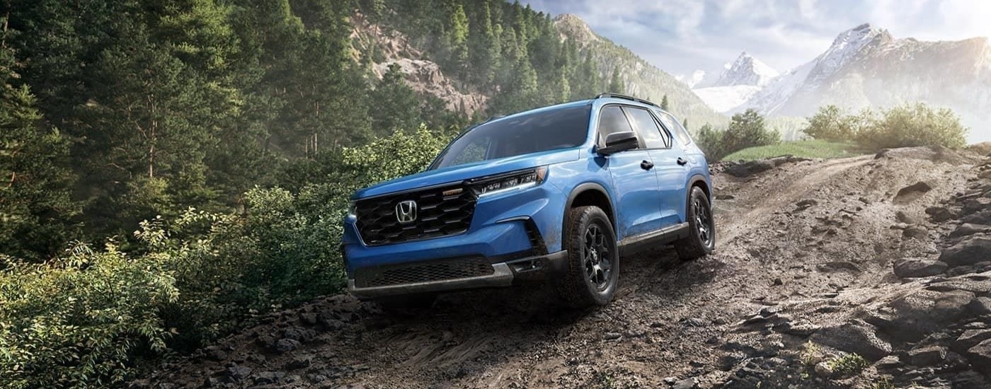 A blue 2023 Honda Pilot Trailsport is shown off-roading.