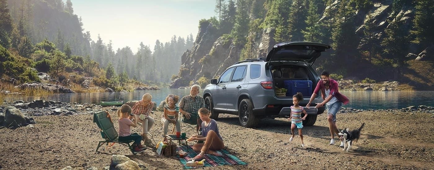 A gray 2023 Honda Pilot Trailsport is shown parked near a lake.