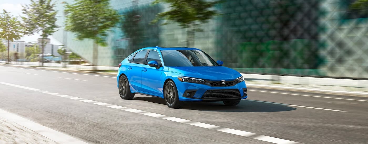 A blue 2024 Honda Civic is shown driving on a city street to visit a Kenmore Honda dealer.