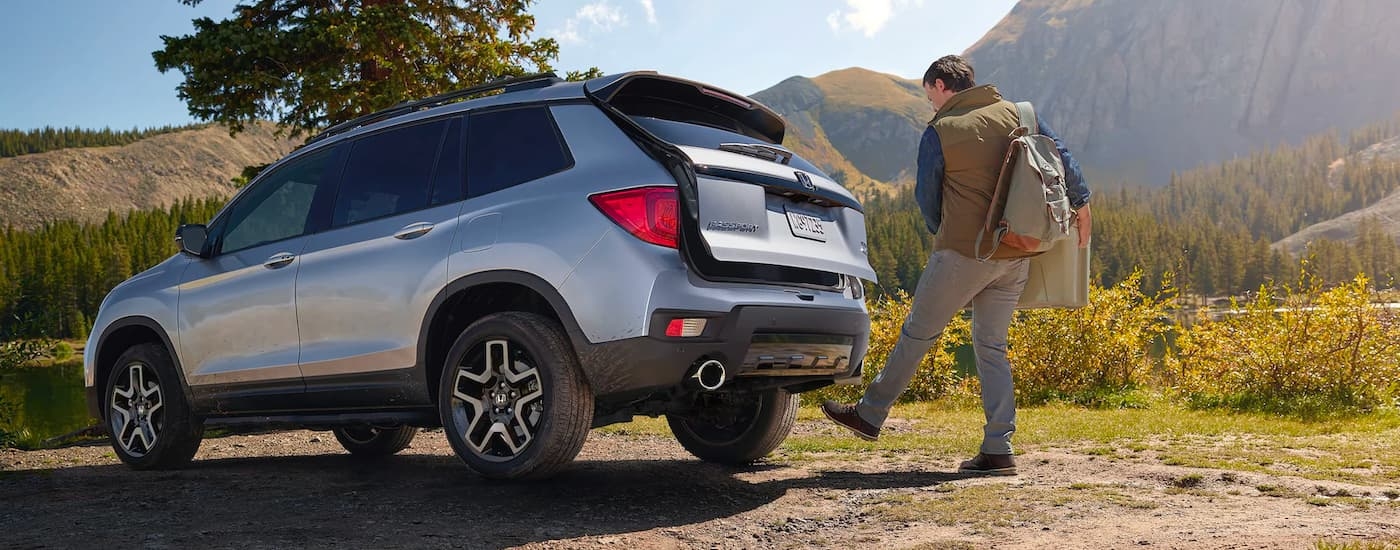 A man is shown opening the rear cargo door on a silver 2023 Honda Passport Elite.