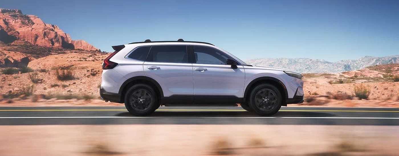 A white 2023 Honda CR-V Sport Touring Hybrid is shown driving on a highway.