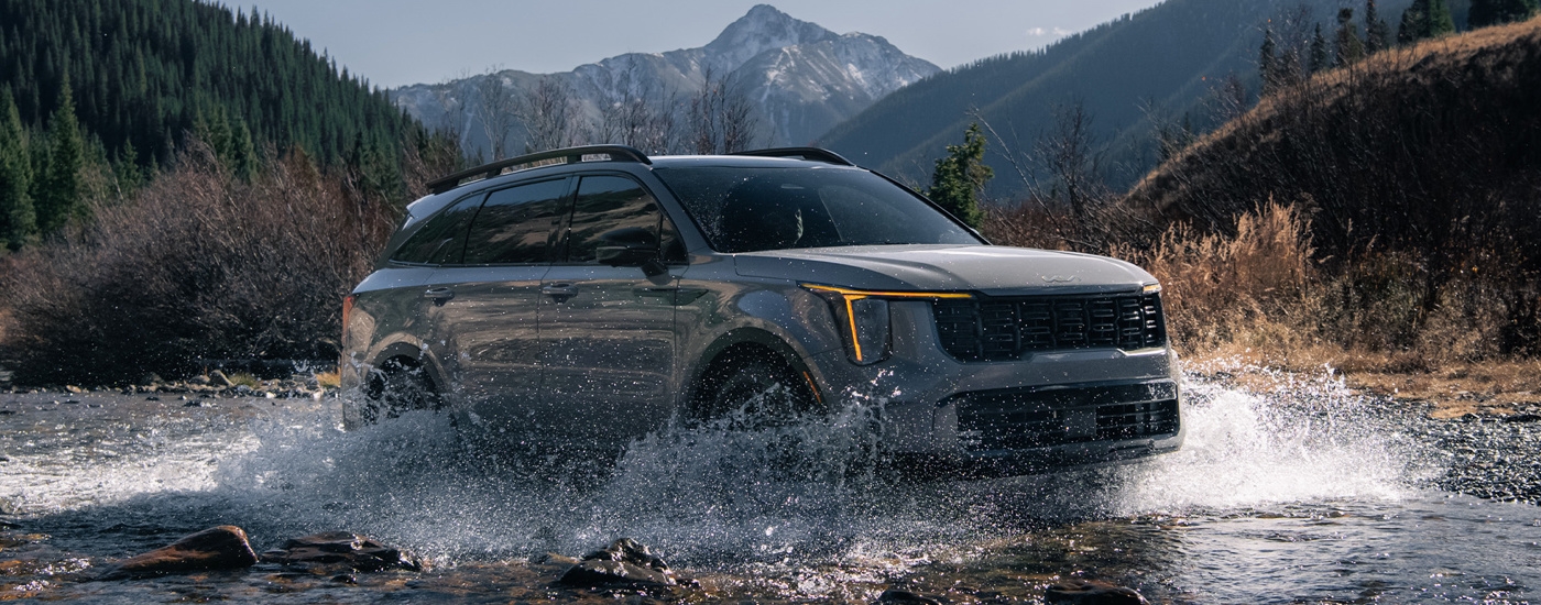 A grey 2024 Kia Sorento X-Pro SX Prestige splashing through water while off-roading.