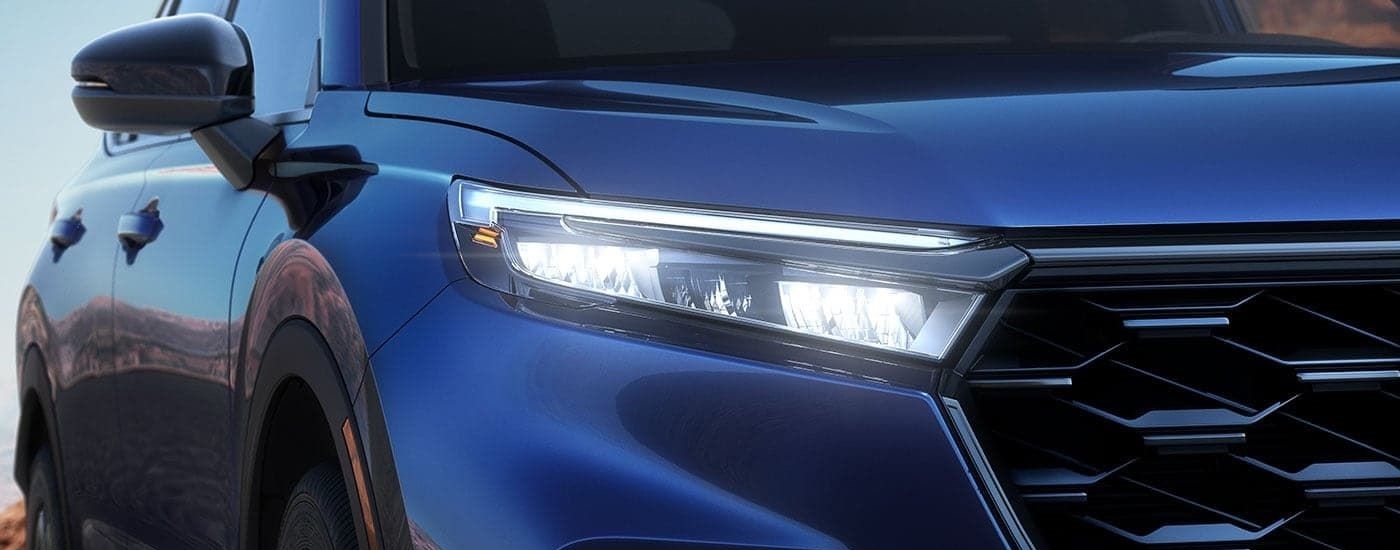 A close up shows the passenger side headlight on a blue 2023 Honda CR-V Sport Touring Hybrid.