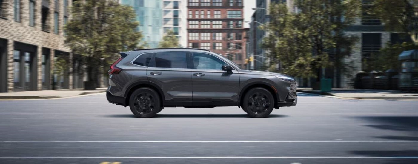 A grey 2024 Honda CR-V is shown from the side driving on a city street.