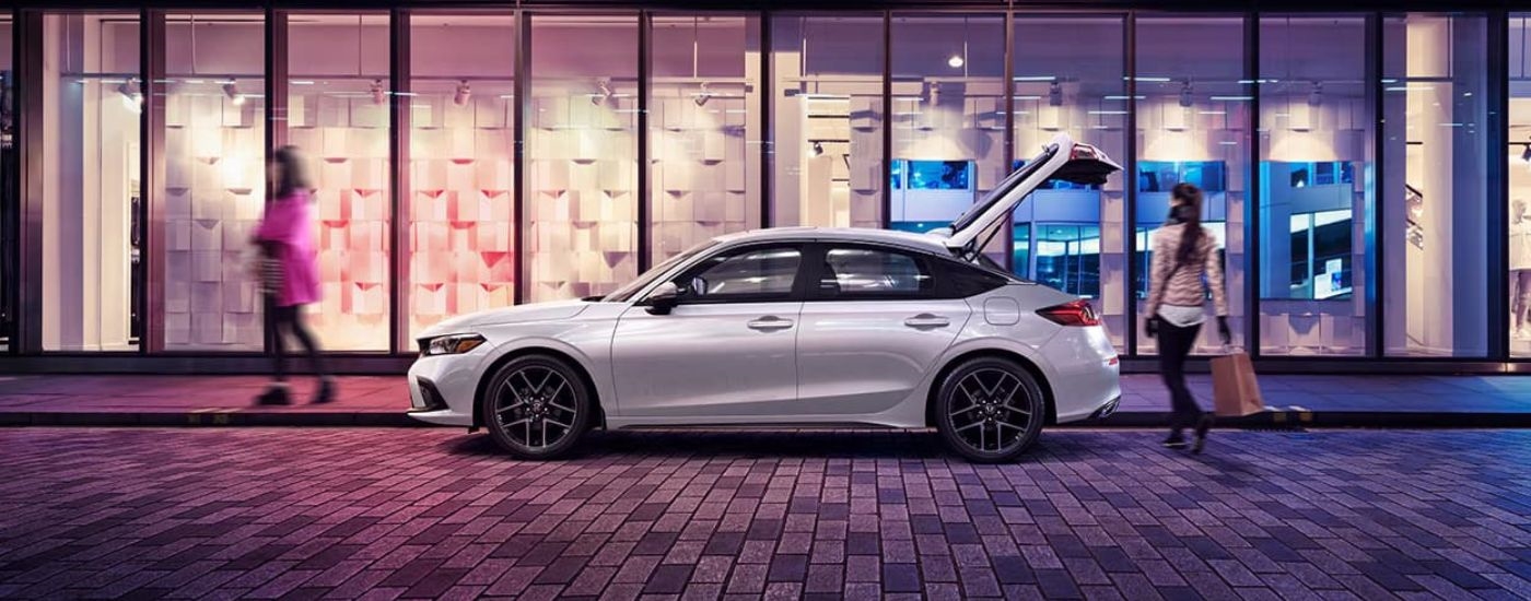 A white 2023 Honda Civic Sport Touring is shown parked outside of a shop.