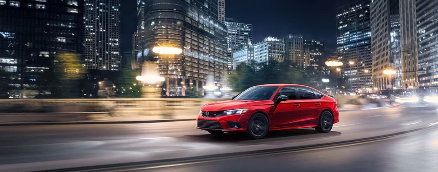 A red 2023 Honda Civic Si is shown on a city street at night after leaving a Honda dealer.