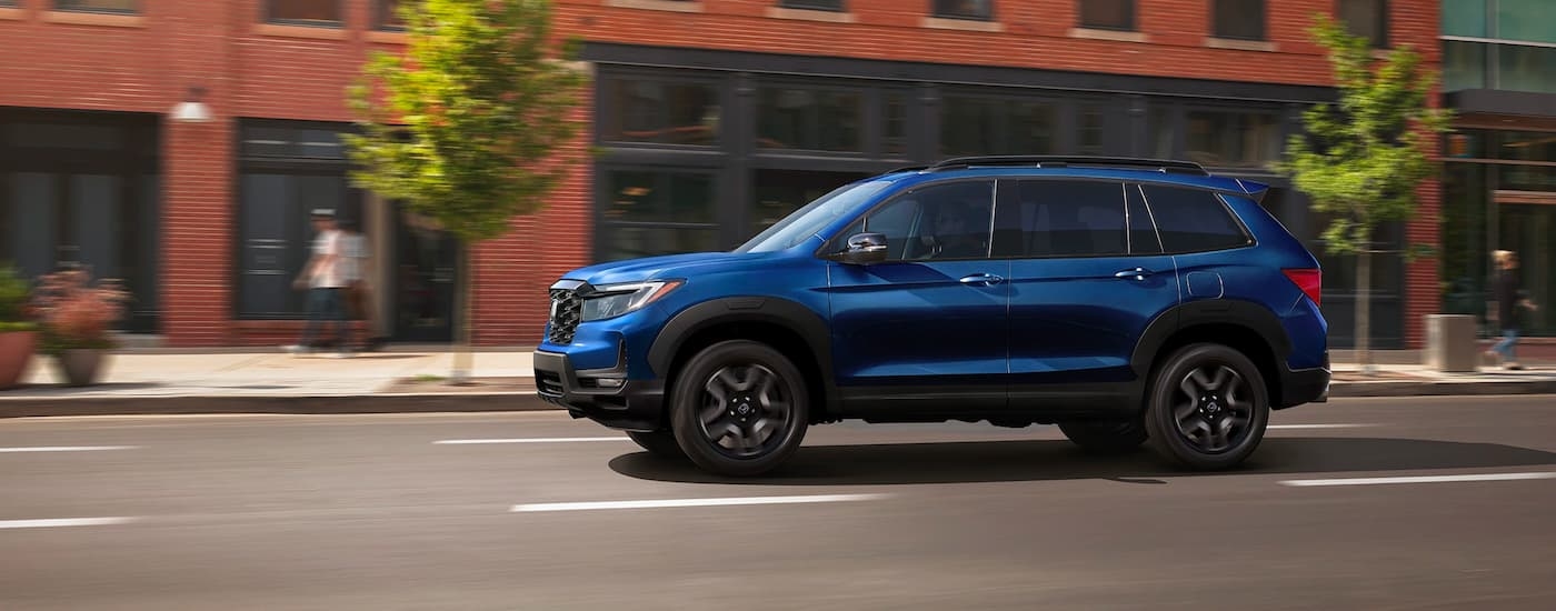 A blue 2023 Honda Passport Elite is shown from the side while driving on a city street.