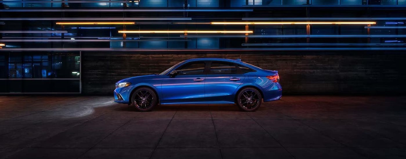 A blue 2024 Honda Civic is shown in front of a building at night.