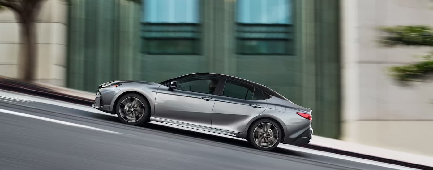 A silver 2025 Toyota Camry is driving up a city hill.