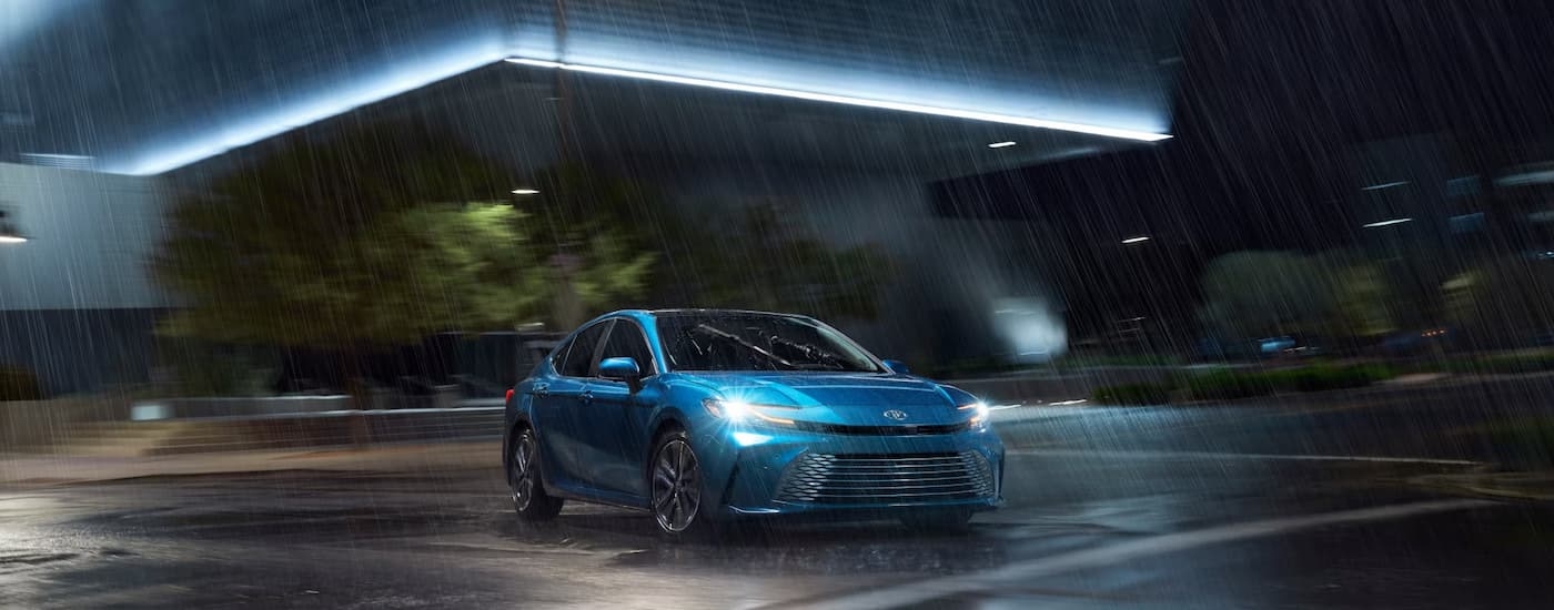 A blue 2025 Toyota Camry XLE is driving on a street at night.