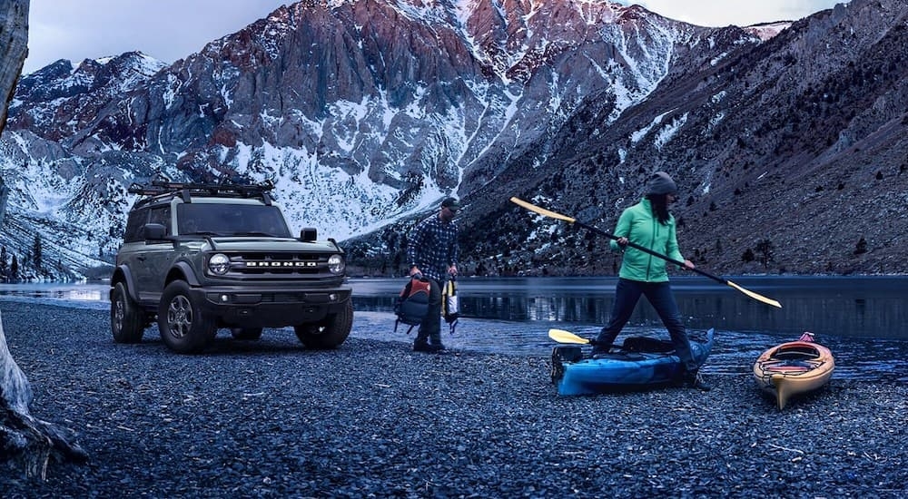 A grey 2024 Ford Bronco parked at a campsite by a lake.