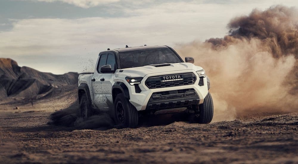 A white 2024 Toyota Tacoma driving off-road in a desert.