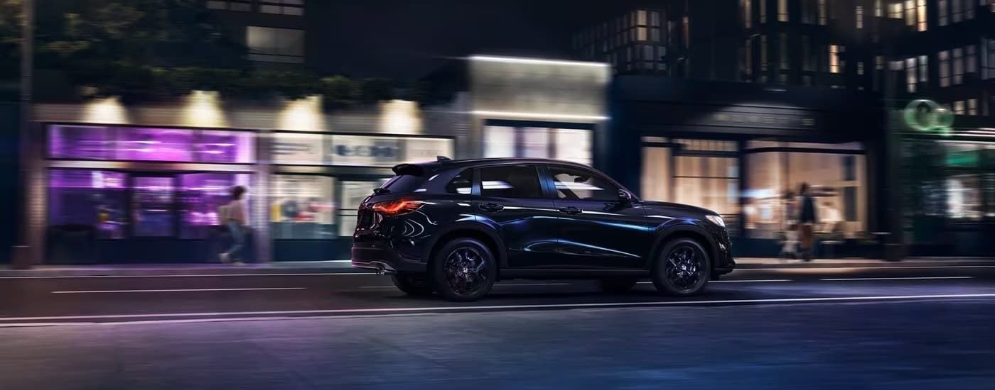 A black 2023 Honda HR-V Sport is shown driving at night on a city street.