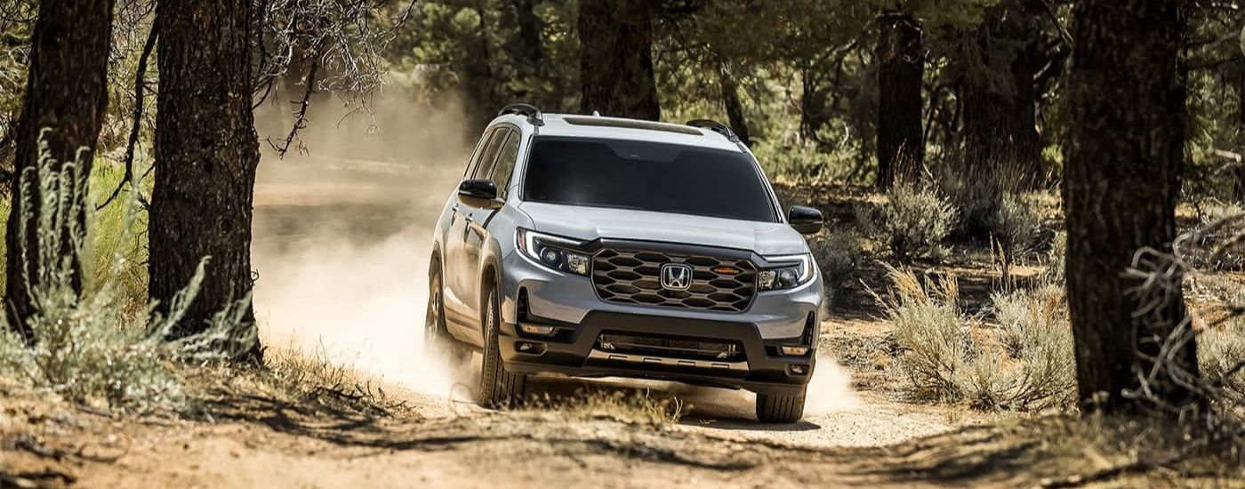 A grey 2024 Honda Passport TrailSport is shown kicking up dust on a trail.