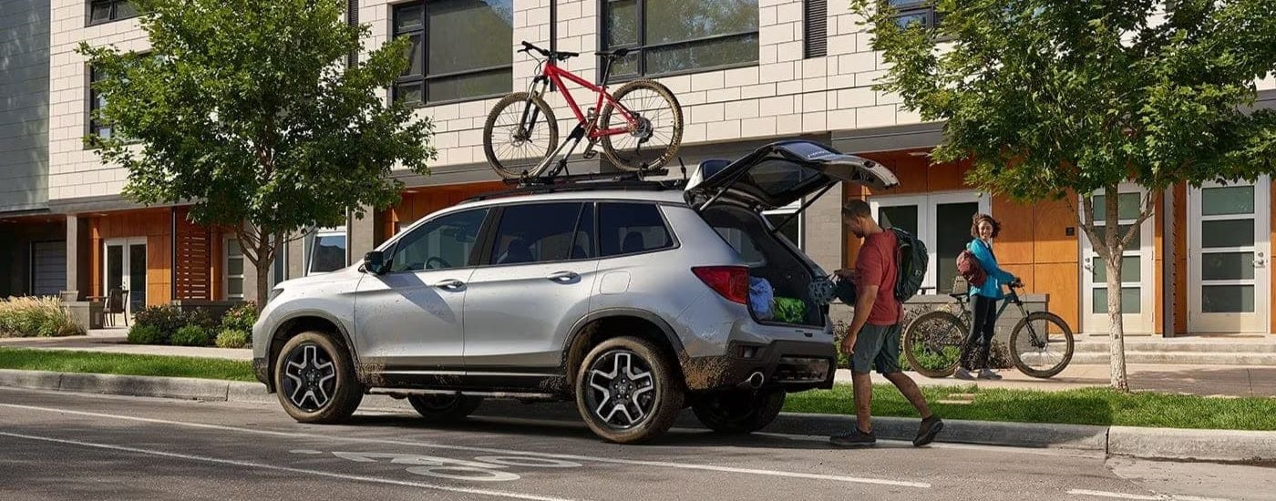 A silver 2024 Honda Passport Elite is shown from the side parked on a city street.