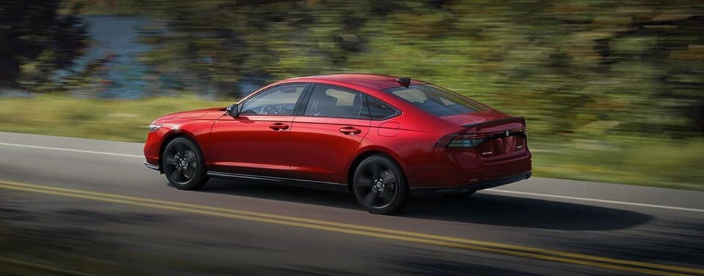 A red 2024 Honda Accord Hybrid is shown driving past a lake.