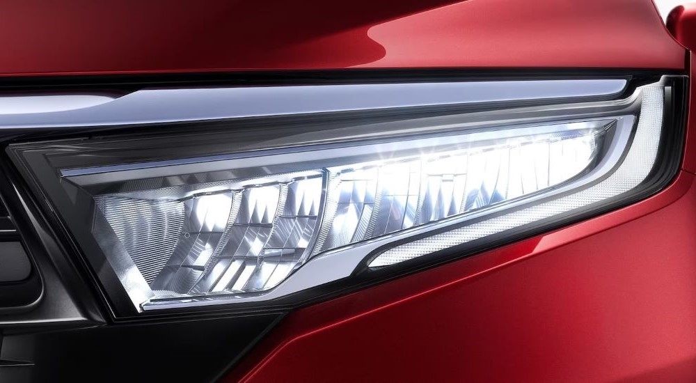 A close up shows the driver side headlight on a red 2024 Honda Odyssey.