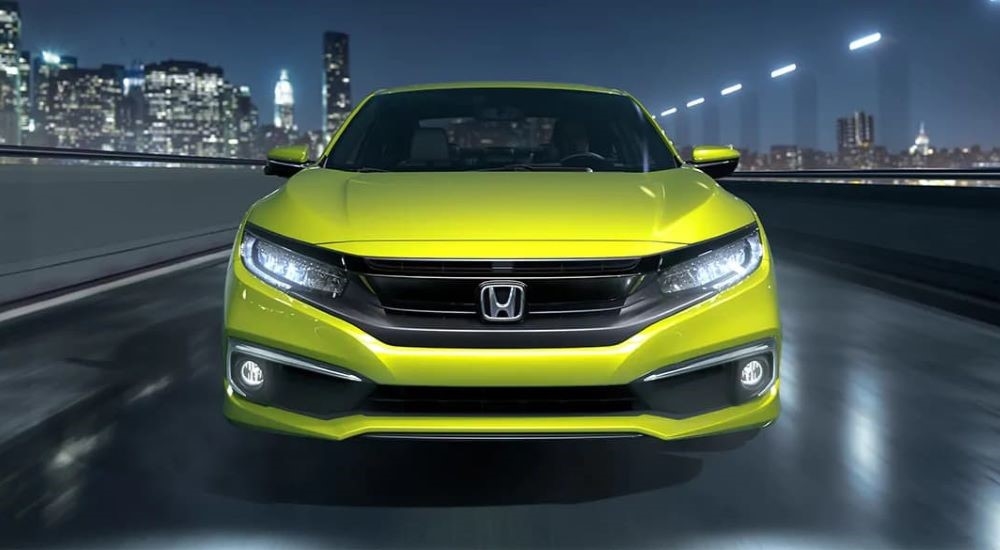 A neon yellow 2019 Honda Civic Touring is shown driving past city buildings at night after visiting used Honda dealer near Kirkland.