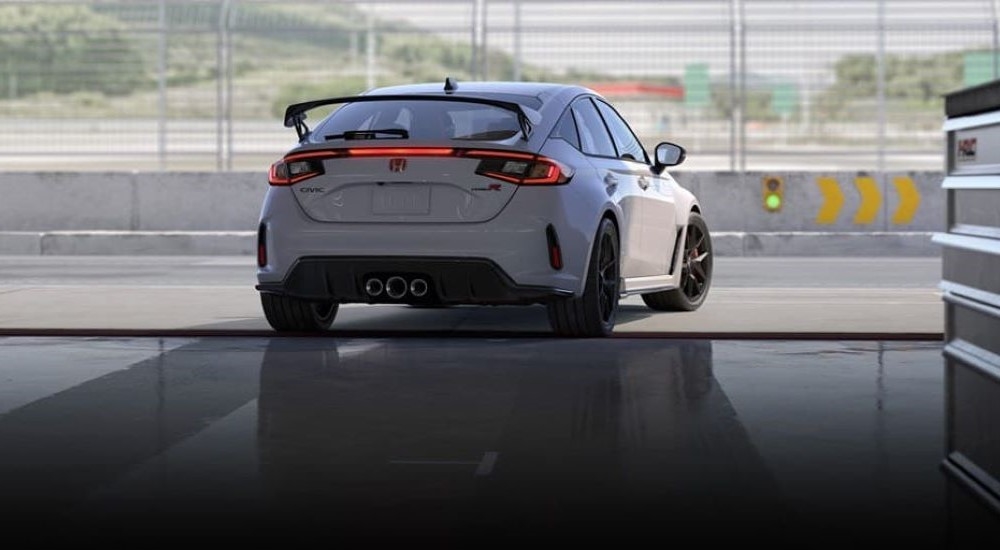 A white 2023 Honda Civic Type R is shown from the rear driving out of a shop.