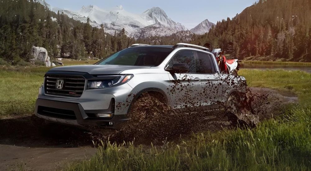 A silver 2023 Honda Ridgeline Sport is shown kicking up mud off-road.