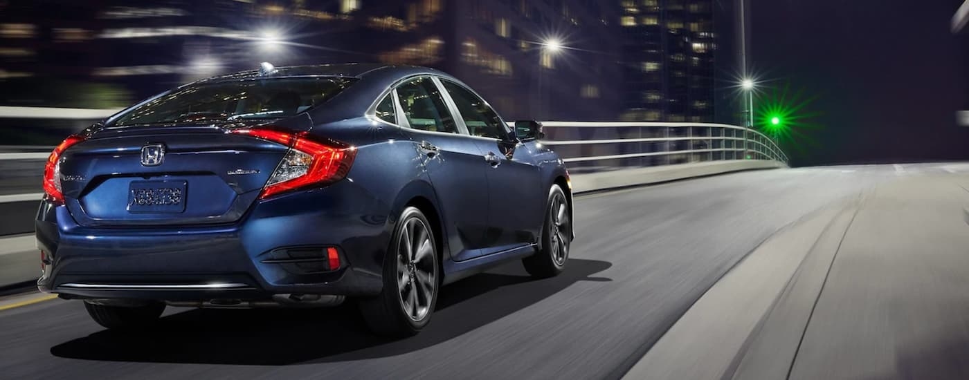 A blue 2020 Honda Civic is shown from the rear on a city street at night.