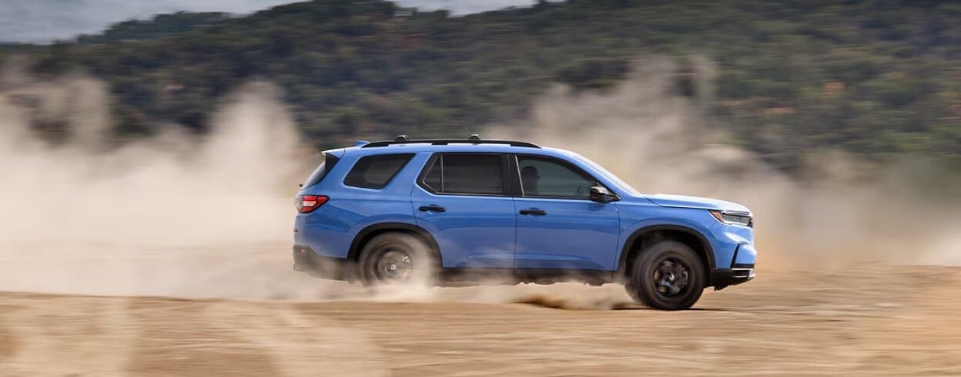 A blue 2023 Honda Pilot TrailSport is shown kicking up dust.