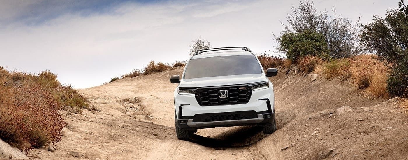 A white Honda Pilot TrailSport is shown driving off-road after viewing a used Honda Pilot for sale.