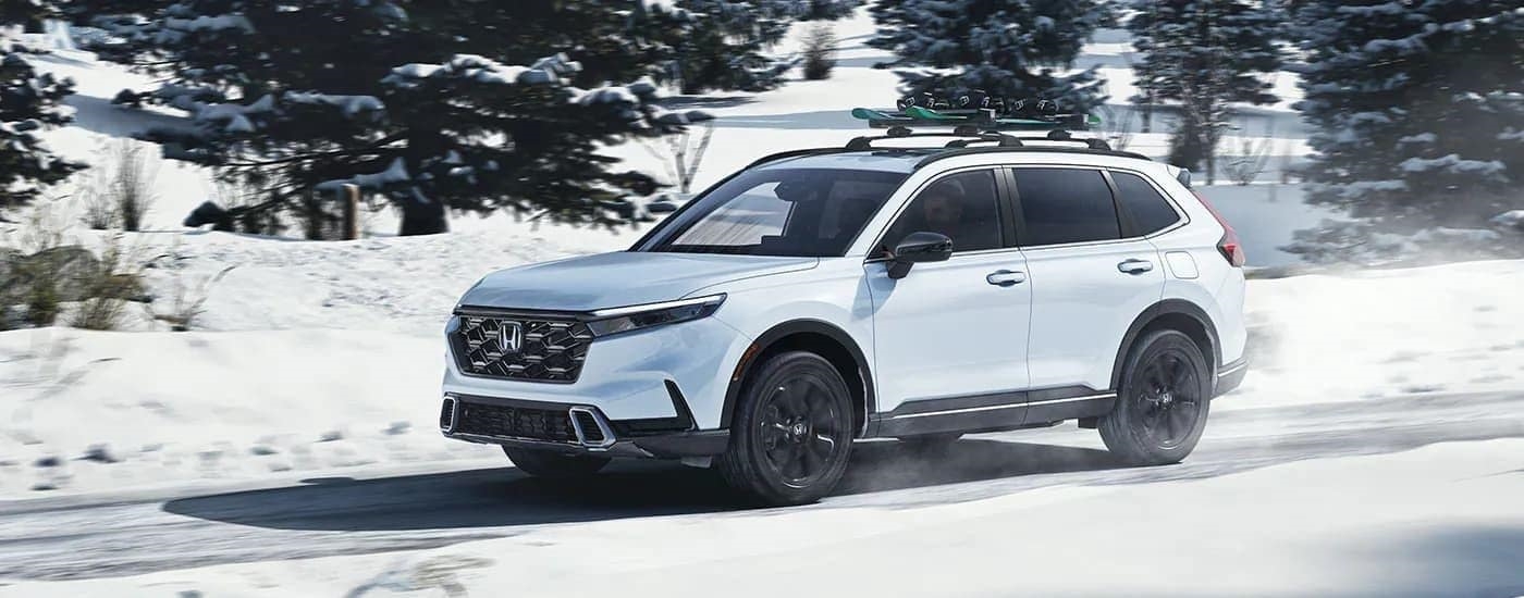 A white 2023 Honda CR-V Sport Touring Hybrid is shown driving on a snowy road.