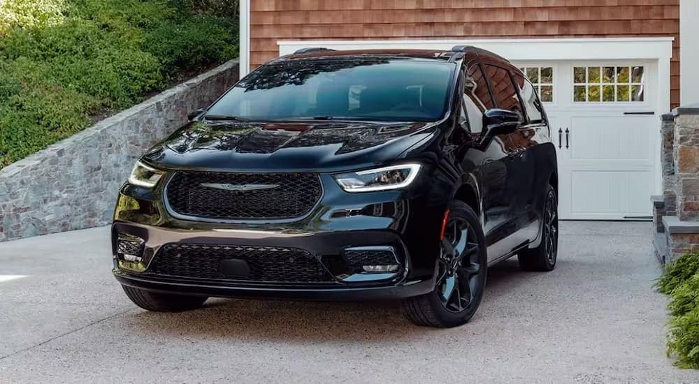 One of the more common used hybrid vehicles for sale, a black 2024 Chrysler Pacifica Hybrid, is shown parked in a driveway.