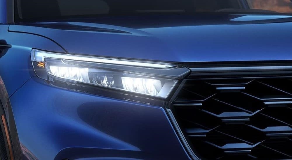 A close-up on the headlight of a blue 2023 Honda CR-V Sport Touring Hybrid is shown.