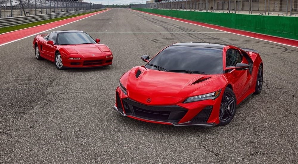 A red 1991 Acura NSX and a red 2022 NSX Type S are shown parked on a racetrack.