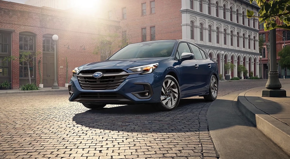 A blue 2025 Subaru Legacy Touring XT driving around a downtown square.