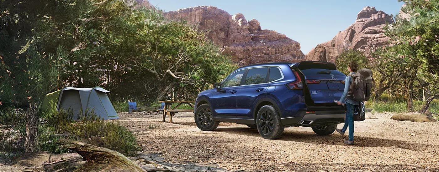A person is shown opening the trunk of a blue 2023 Honda CR-V Sport Touring Hybrid.