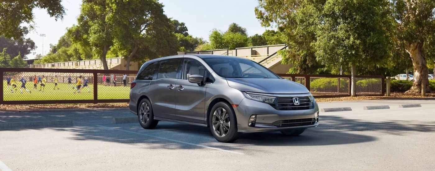 A silver 2024 Honda Odyssey Elite is shown parked near a soccer field.