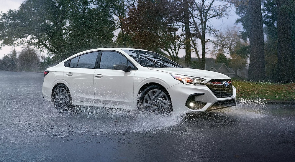 A white 2025 Subaru Legacy Sport driving through a puddle in the rain.