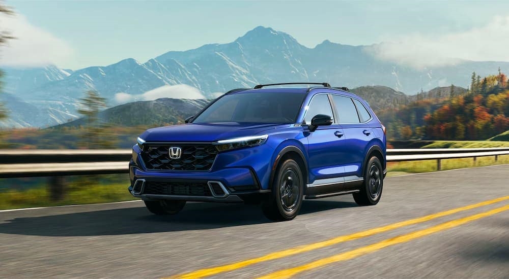 A blue 2023 Honda CR-V Hybrid Sport Touring is shown driving on an open road after leaving a Honda dealer near you.