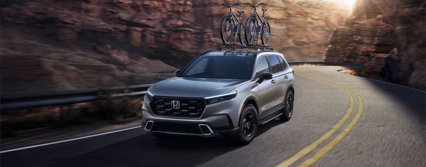 A silver 2023 Honda CR-V Hybrid is shown driving on a canyon road with bikes.