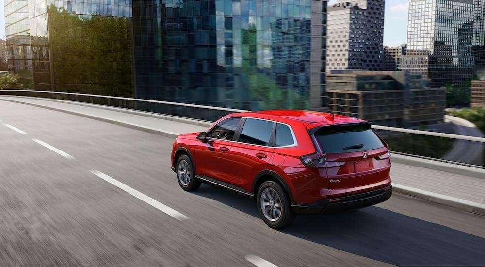 A red 2023 Honda CR-V EX is shown from a rear angle driving on an open highway after leaving a Honda dealer near Lynnwood, WA.