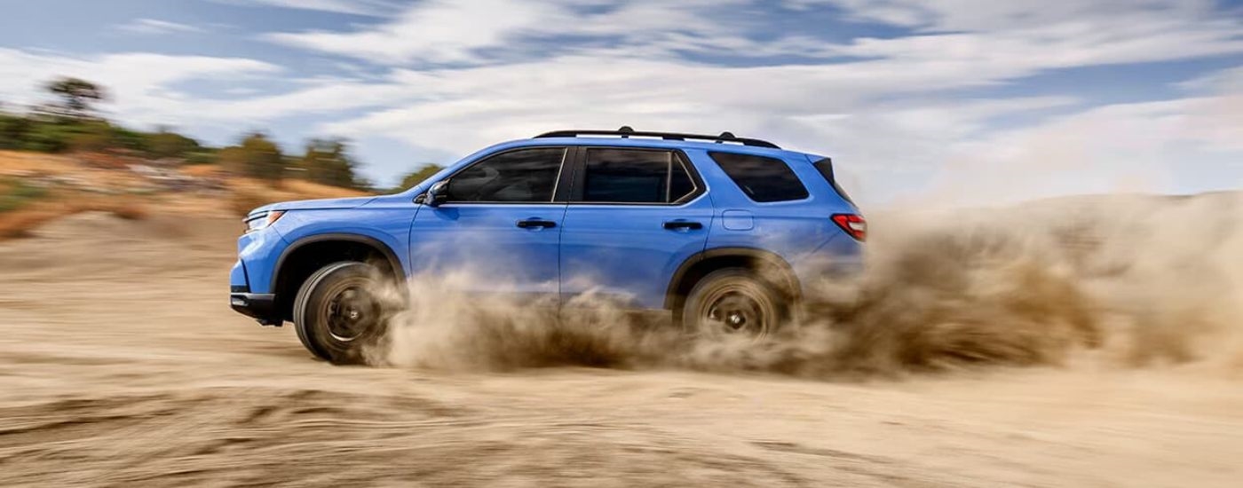 A blue 2024 Honda Pilot Trailsport is shown kicking up dust.