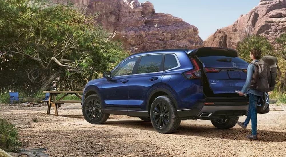 A blue 2024 Honda CR-V Sport Touring Hybrid is shown parked near a picnic table.