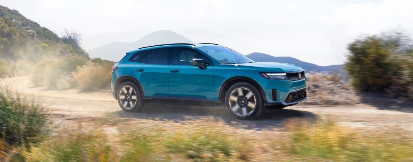 A blue 2024 Honda Prologue Elite is shown from the side driving on a dirt road.