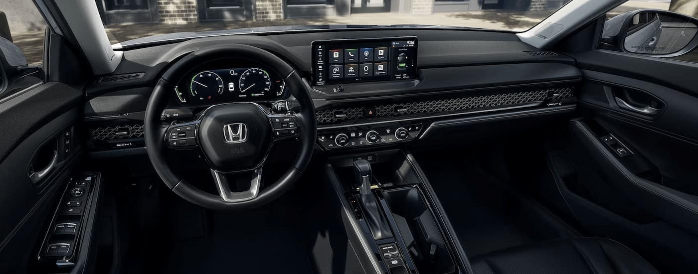The black interior of a 2023 Honda Accord Touring Hybrid shows the steering wheel and center console.