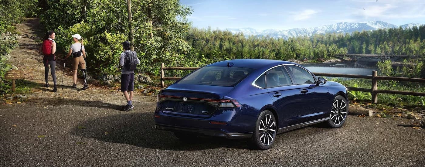 A blue 2023 Honda Accord Touring Hybrid is shown from the rear while parked in a hiking trail lot.