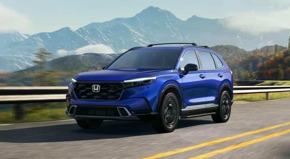 A blue 2024 Honda CR-V ST Hybrid is shown driving to a Redmond Honda dealer.