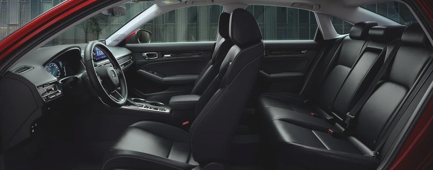 The black interior of a 2023 Honda Civic Touring shows two rows of seating and the steering wheel.